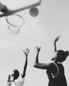 Players reaching up toward a basketball hoop during a game.